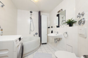 Das zeitlose Badezimmer besitzt eine große Eckbadewanne und genügend Platz für die Waschmaschine.